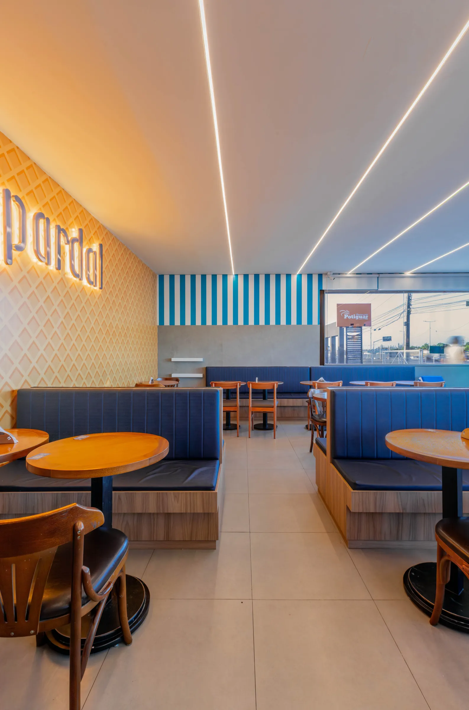 Salão da sorveteria Pardal com bancos estofados azuis, parede de listras azul e branco, logo iluminado e vitrine voltada para a rua