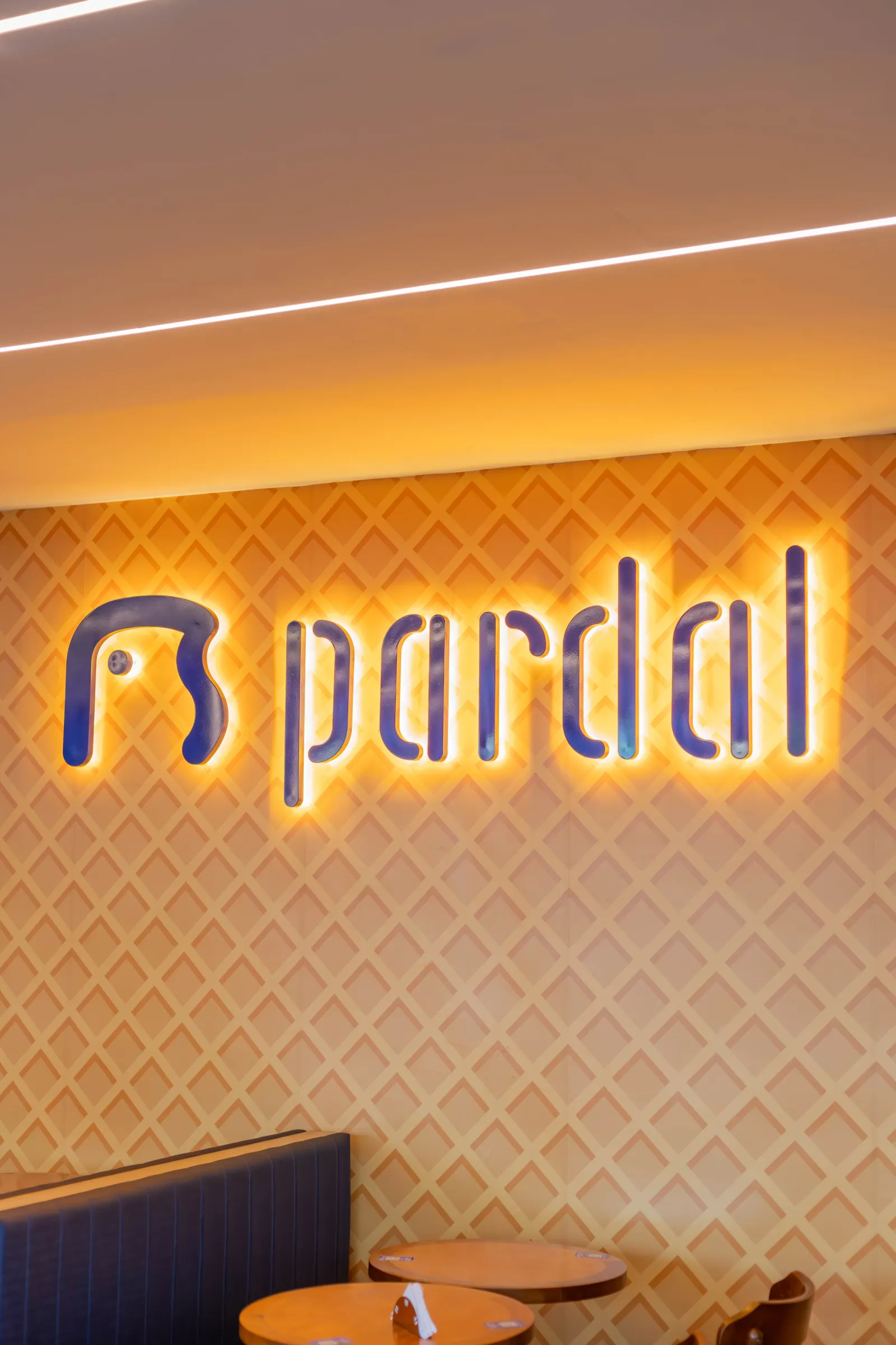 Detalhe do logo iluminado da Pardal sobre parede texturizada de casquinha de sorvete, ao lado de banco azul