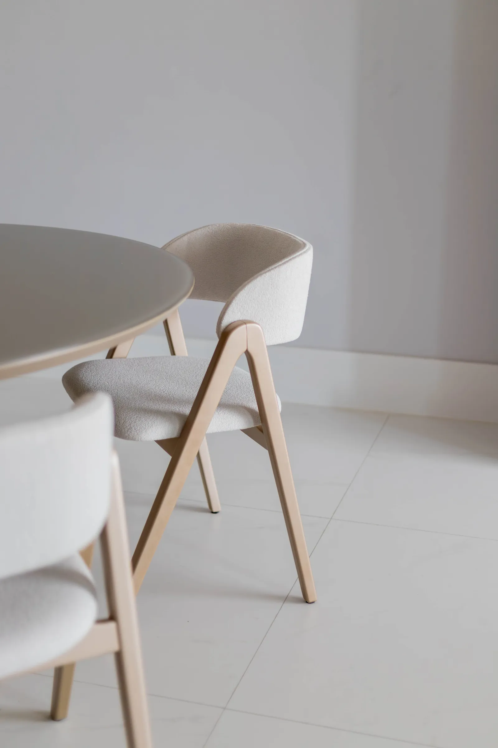 Detalhe das cadeiras de jantar do Residencial ML em bouclé creme com estrutura de madeira clara, junto à mesa redonda