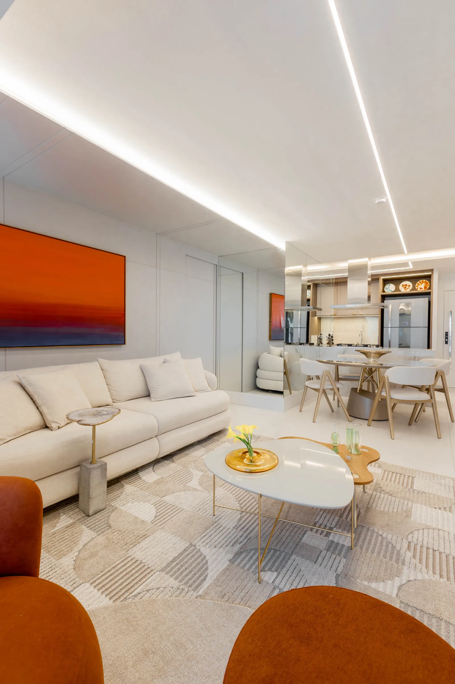 Living do Residencial ML com sofá bege e grande quadro abstrato laranja e azul, integrado à sala de jantar e à cozinha com painel espelhado ao fundo