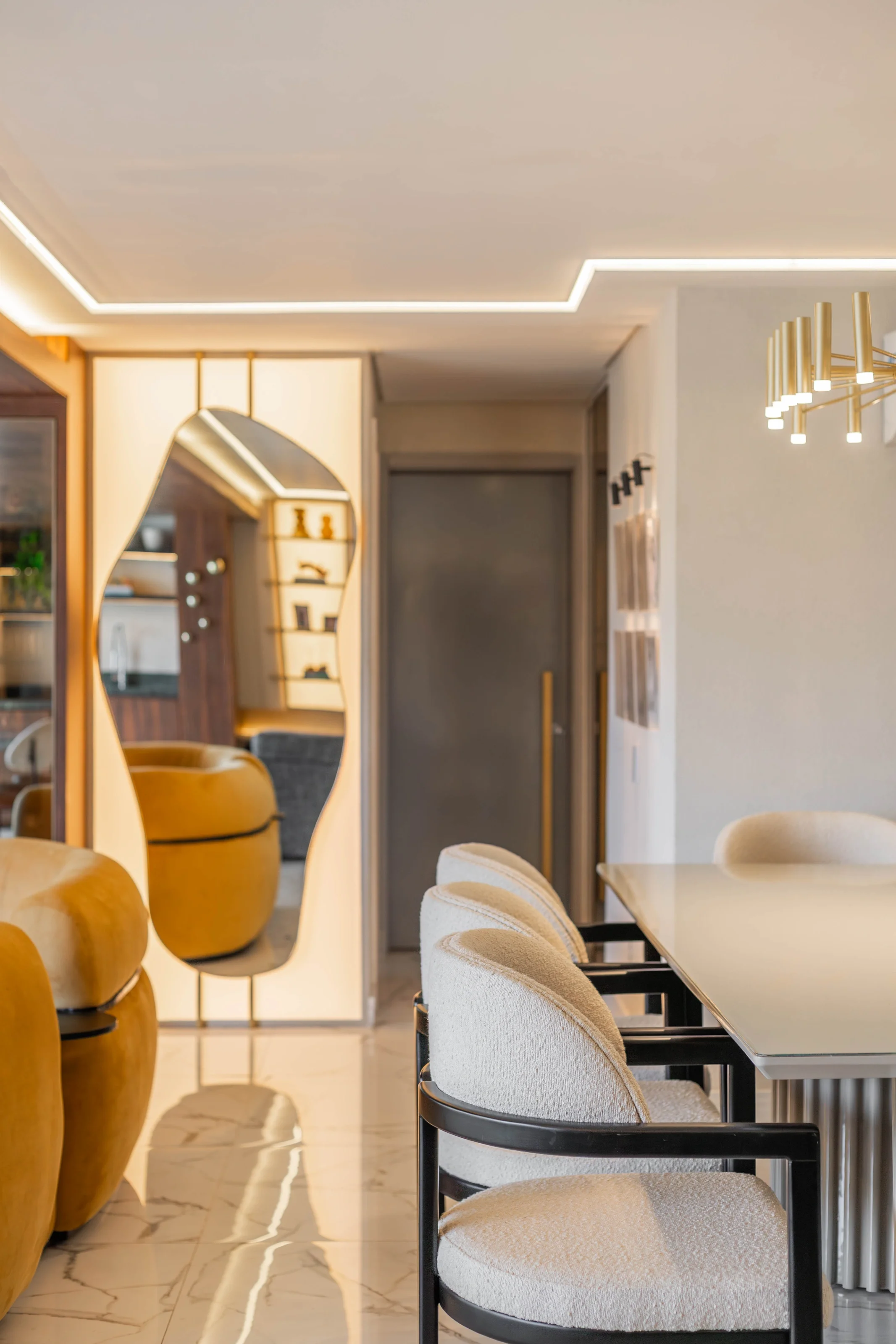 Sala de jantar do Residencial PL com mesa branca e cadeiras de bouclé creme com estrutura preta, espelho orgânico iluminado, poltronas mostarda e lustre dourado tubular
