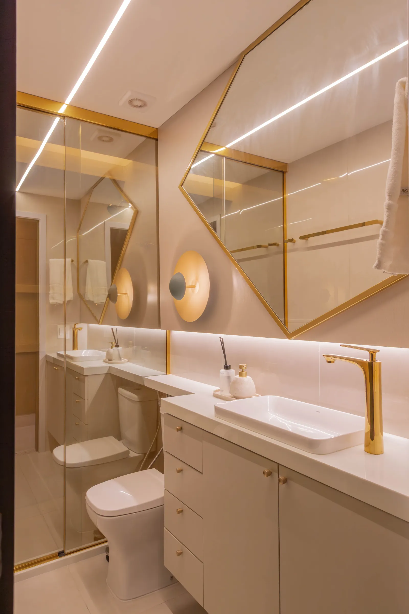 Lavabo do Residencial TN em tons nude com detalhes dourados, cuba de apoio, torneira e espelho octogonal com moldura dourada