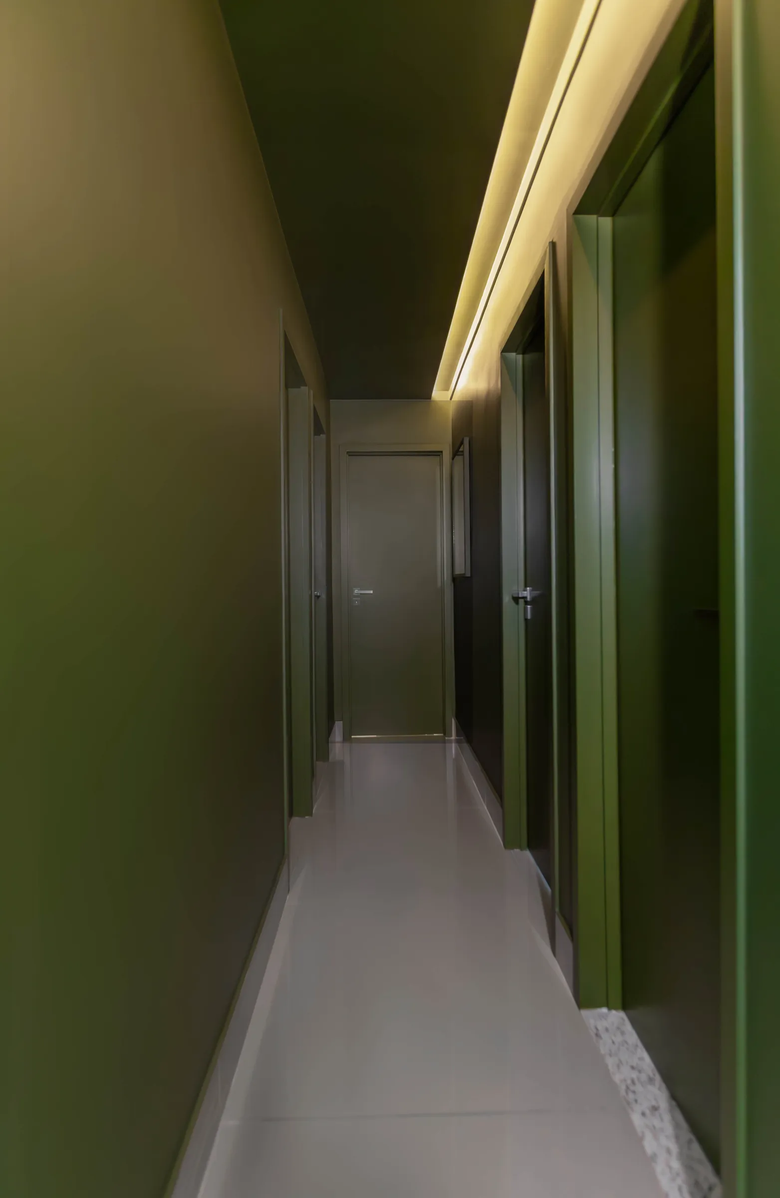 Corredor do Residencial TN com paredes verde-oliva, portas embutidas e iluminação indireta de sanca sobre piso porcelanato claro