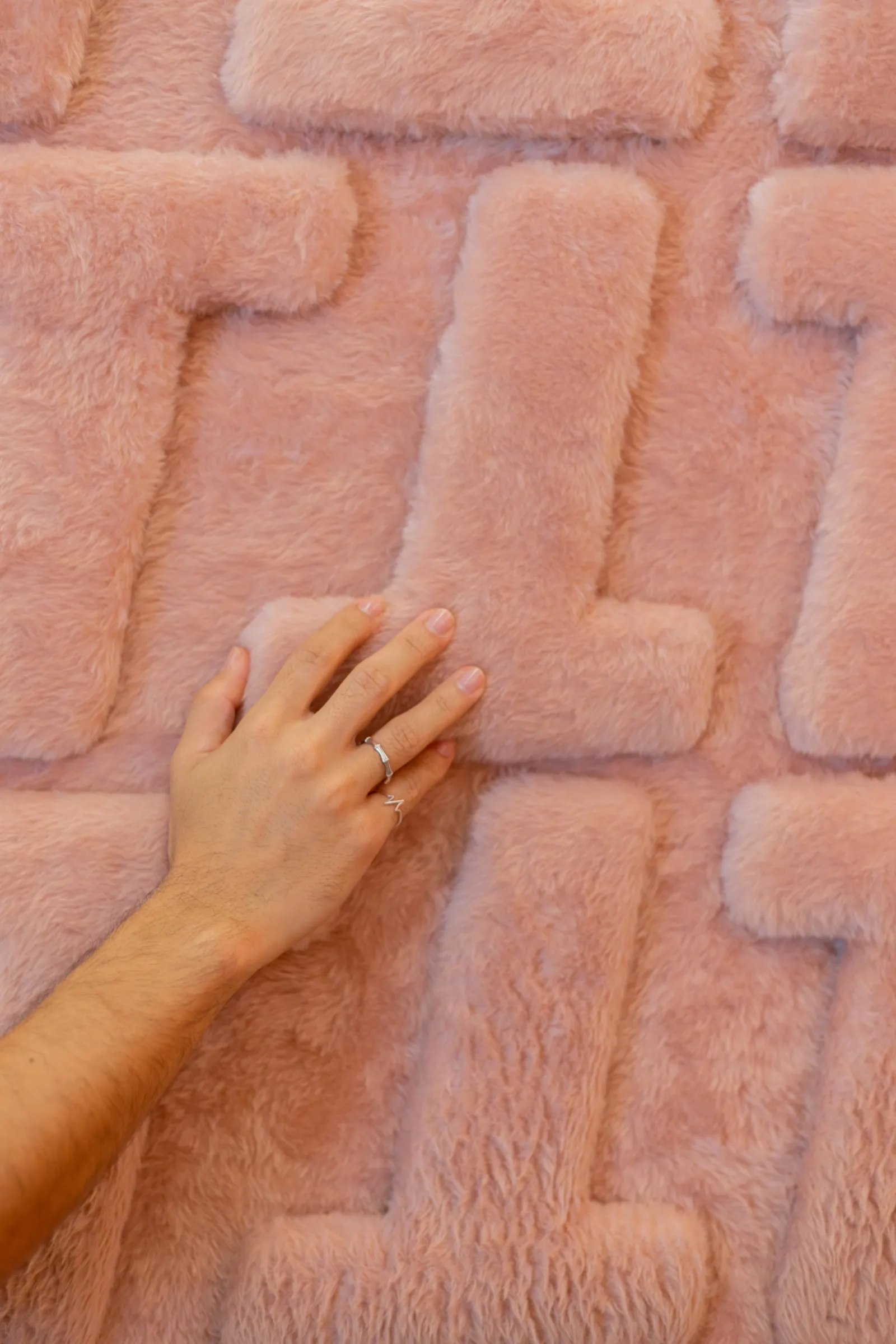 Corredor da loja Teca com divisória de lâminas espelhadas, parede de pelúcia terracota com moldura de LED e balcão cilíndrico de latão iluminado ao fundo